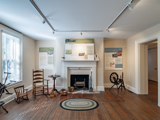 Historic interior room with fireplace, exhibits, and wooden chairs